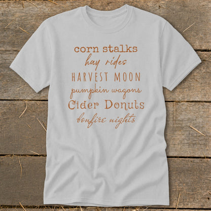 Light gray t-shirt with fall phrases: corn stalks, hay rides, harvest moon, pumpkin wagons, cider donuts, bonfire nights.