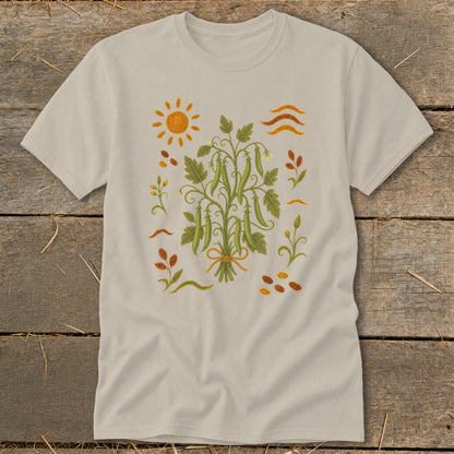 T-shirt with embroidered peas, sun, and scattered leaves and seeds.