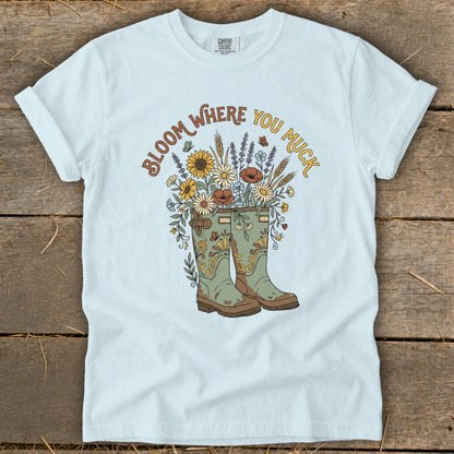 Light blue t-shirt with green boots, flowers, butterflies and text "Bloom Where You Muck".