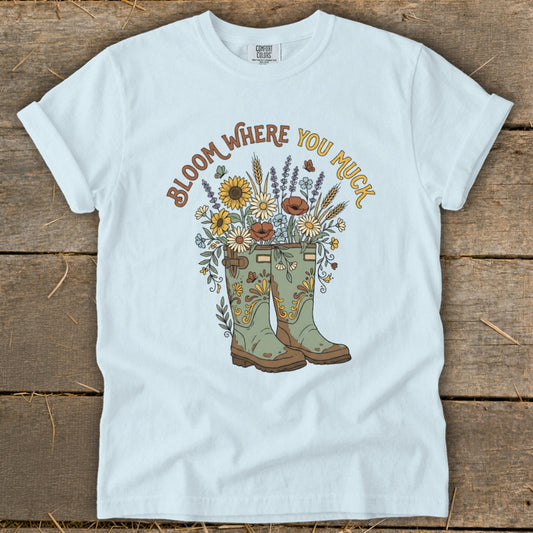 Light blue t-shirt with green boots, flowers, butterflies and text "Bloom Where You Muck".