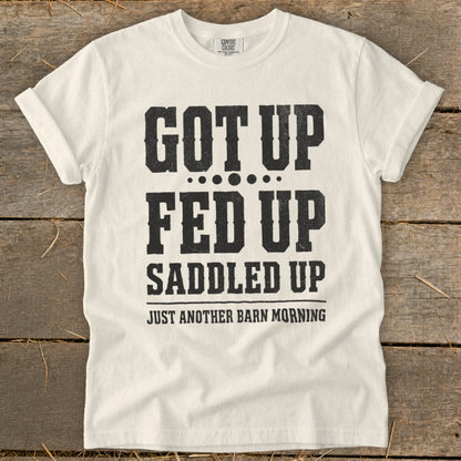 White t-shirt with black text: "GOT UP FED UP SADDLED UP JUST ANOTHER BARN MORNING"