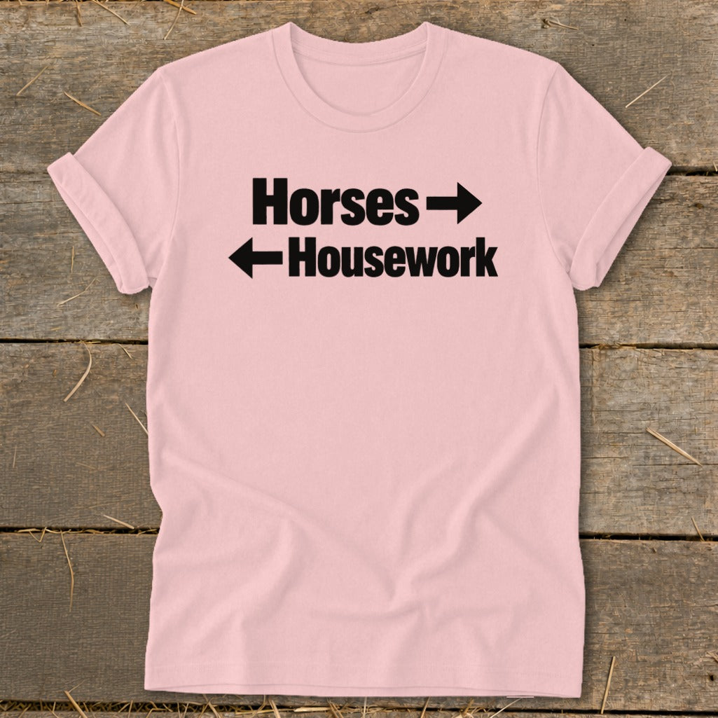 A light pink t-shirt with rolled-up sleeves displays black text that reads "Horses" with a right-pointing arrow above "Housework" with a left-pointing arrow.