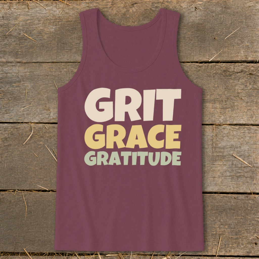 A maroon tank top featuring the text GRIT GRACE GRATITUDE centered on a wooden background.