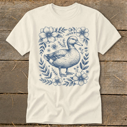 Cream t-shirt with a blue line drawing of a duck surrounded by flowers and leaves.