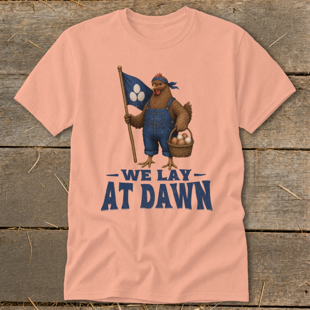 Peach t-shirt with a chicken in overalls holding a flag and basket of eggs with text "WE LAY AT DAWN".