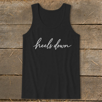 Black tank top with white cursive text "heels down" against wooden background.