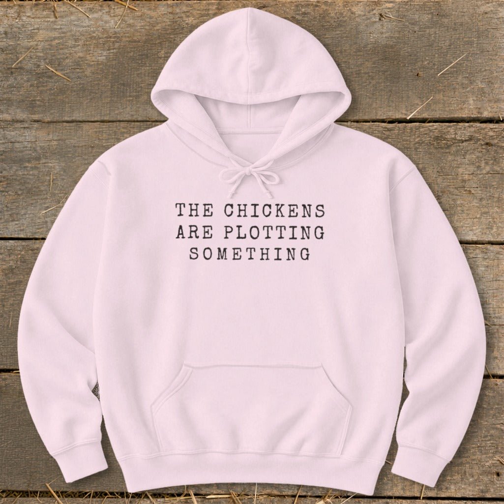 Light pink hoodie with black text reading "THE CHICKENS ARE PLOTTING SOMETHING".