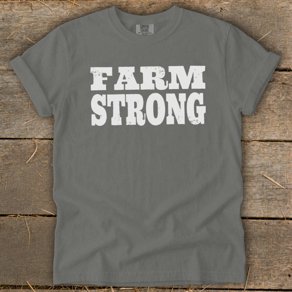 A grey t-shirt featuring the distressed white text "FARM STRONG" laid flat on a wooden surface.