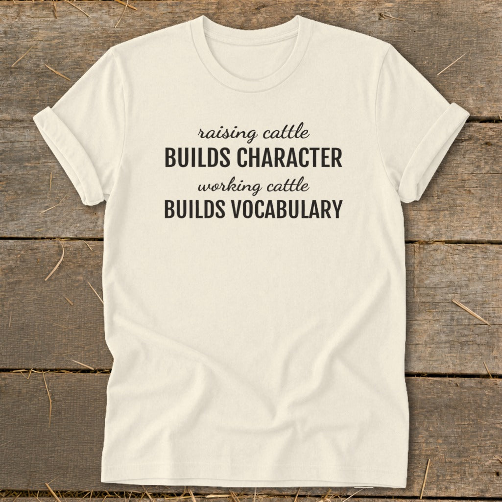 Cream t-shirt with black text: "raising cattle BUILDS CHARACTER working cattle BUILDS VOCABULARY"
