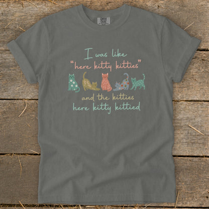 T-shirt with text "here kitty kitties" and colorful cartoon cats.