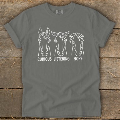 A dark grey t-shirt featuring three horse face line drawings with captions reading curious, listening, and nope.