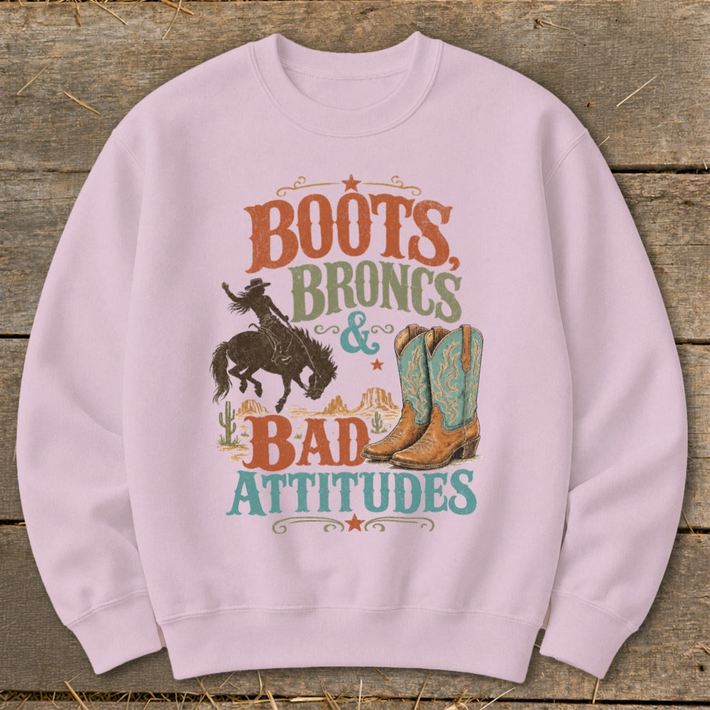 Pink sweatshirt with "Boots, Broncs & Bad Attitudes" graphic featuring a bronco rider and cowboy boots.