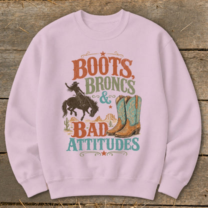 Pink sweatshirt with "Boots, Broncs & Bad Attitudes" graphic featuring a bronco rider and cowboy boots.