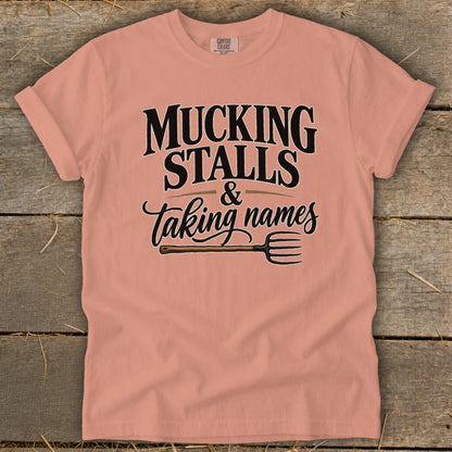 Peach t-shirt with "Mucking stalls & taking names" text and a pitchfork graphic.