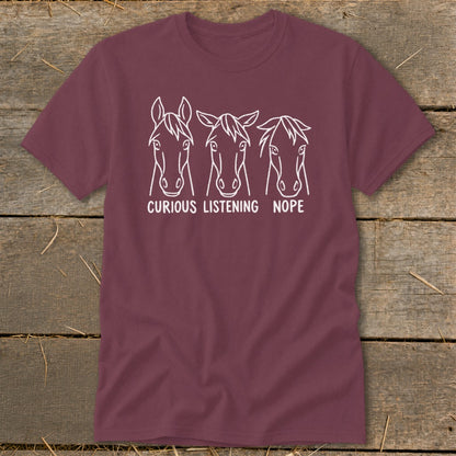 Maroon t-shirt featuring three horse heads with varying ear positions labeled curious, listening, and nope.