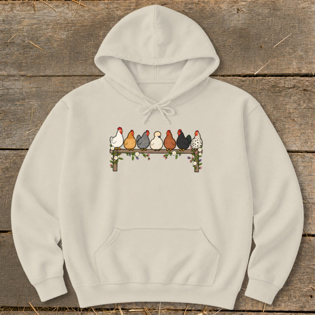 A cream-colored hoodie featuring an illustration of seven colorful chickens perched on a flower-decorated wooden fence.