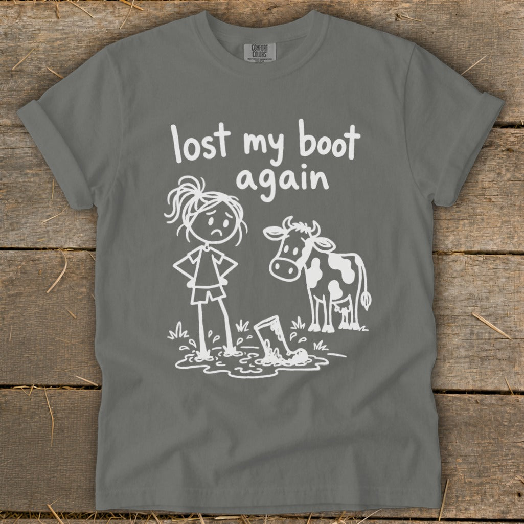 A grey t-shirt featuring a white graphic of a cow, a sad girl standing in a puddle, and the text lost my boot again.