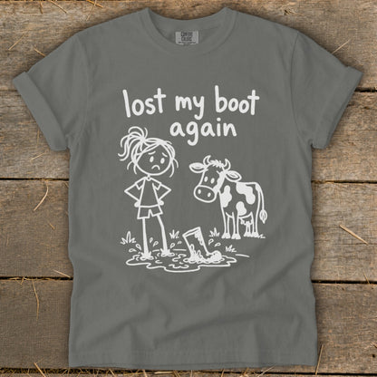 A grey t-shirt featuring a white graphic of a cow, a sad girl standing in a puddle, and the text lost my boot again.