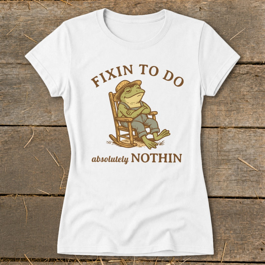 White t-shirt with a frog in a rocking chair wearing overalls and a hat, text says "FIXIN TO DO absolutely NOTHIN".