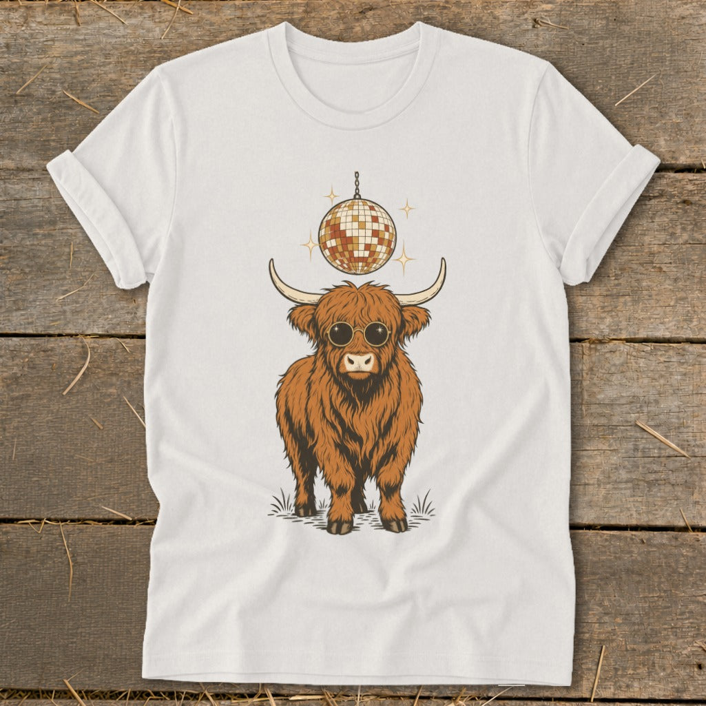 Highland cow with sunglasses stands under a disco ball on a white t-shirt.