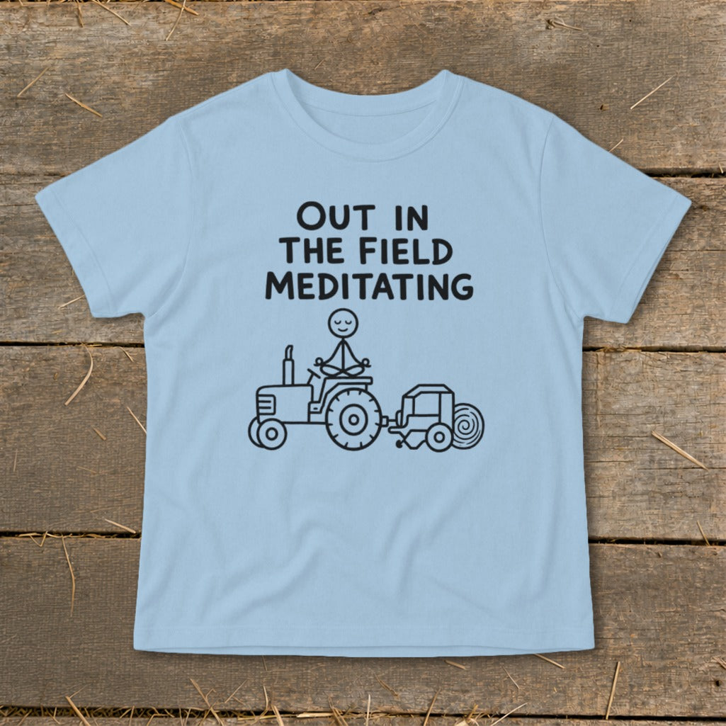 Light blue t-shirt with "Out in the Field Meditating" text and stick figure on tractor graphic.