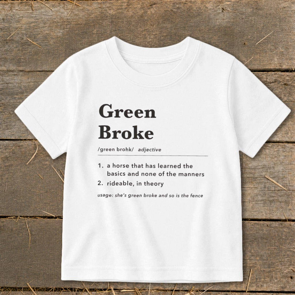 White t-shirt featuring black dictionary-style text defining Green Broke laid on wooden background.