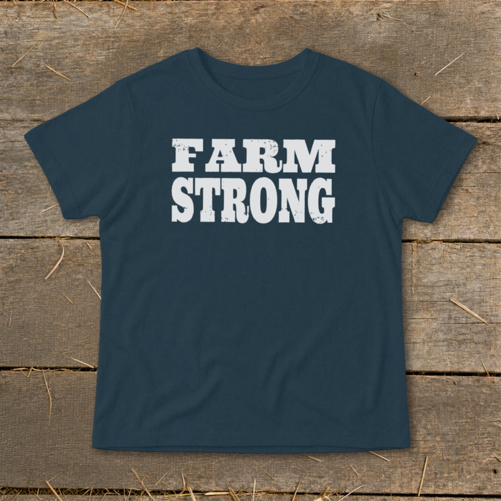 Dark blue short-sleeve t-shirt with distressed white text reading FARM STRONG, displayed on rustic wood.