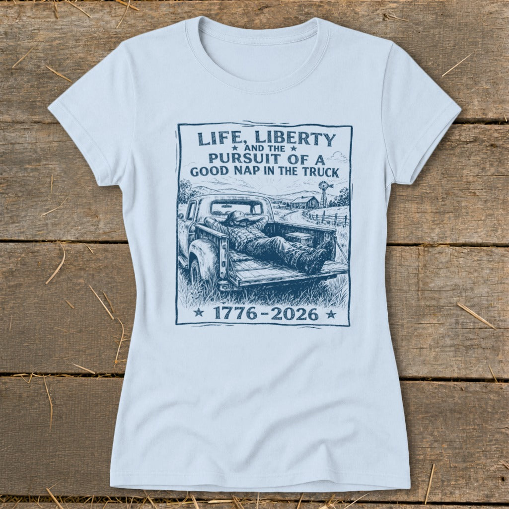 Light blue t-shirt with graphic of man napping in truck bed, reads "Life, Liberty and the Pursuit of a Good Nap in the Truck 1776-2026".