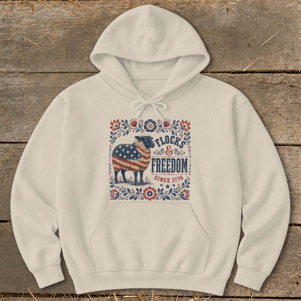 Cream hoodie with a sheep design, American flag, and text "FLOCKS & FREEDOM SINCE 1776".