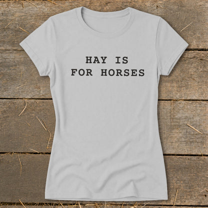 Grey t-shirt with black text "HAY IS FOR HORSES" on rustic wood background.