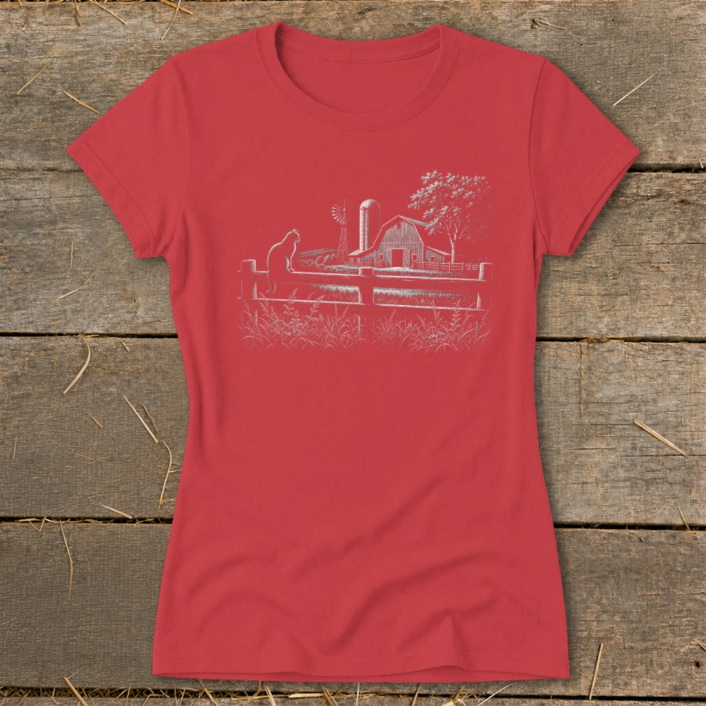 Red t-shirt with a white line drawing of a cat on a fence, barn, windmill, and tree.