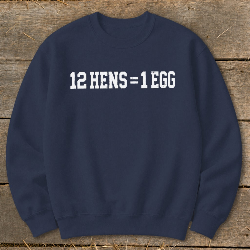 Dark blue crewneck sweatshirt featuring the white distressed text 12 HENS = 1 EGG on the chest, laid flat on wooden planks.