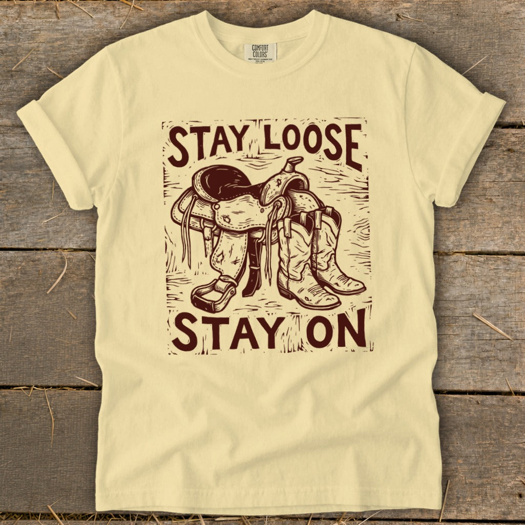 Yellow t-shirt with maroon graphic of a saddle and cowboy boots, saying "STAY LOOSE STAY ON".