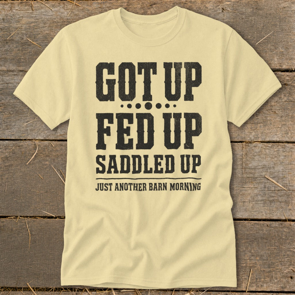 Light yellow t-shirt with black text reading "GOT UP FED UP SADDLED UP JUST ANOTHER BARN MORNING".