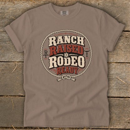 Taupe t-shirt featuring a circular western graphic with the text Ranch Raised Rodeo Ready.