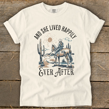 T-shirt graphic with desert scene, cowgirl on horse, and text "And She Lived Happily Ever After".