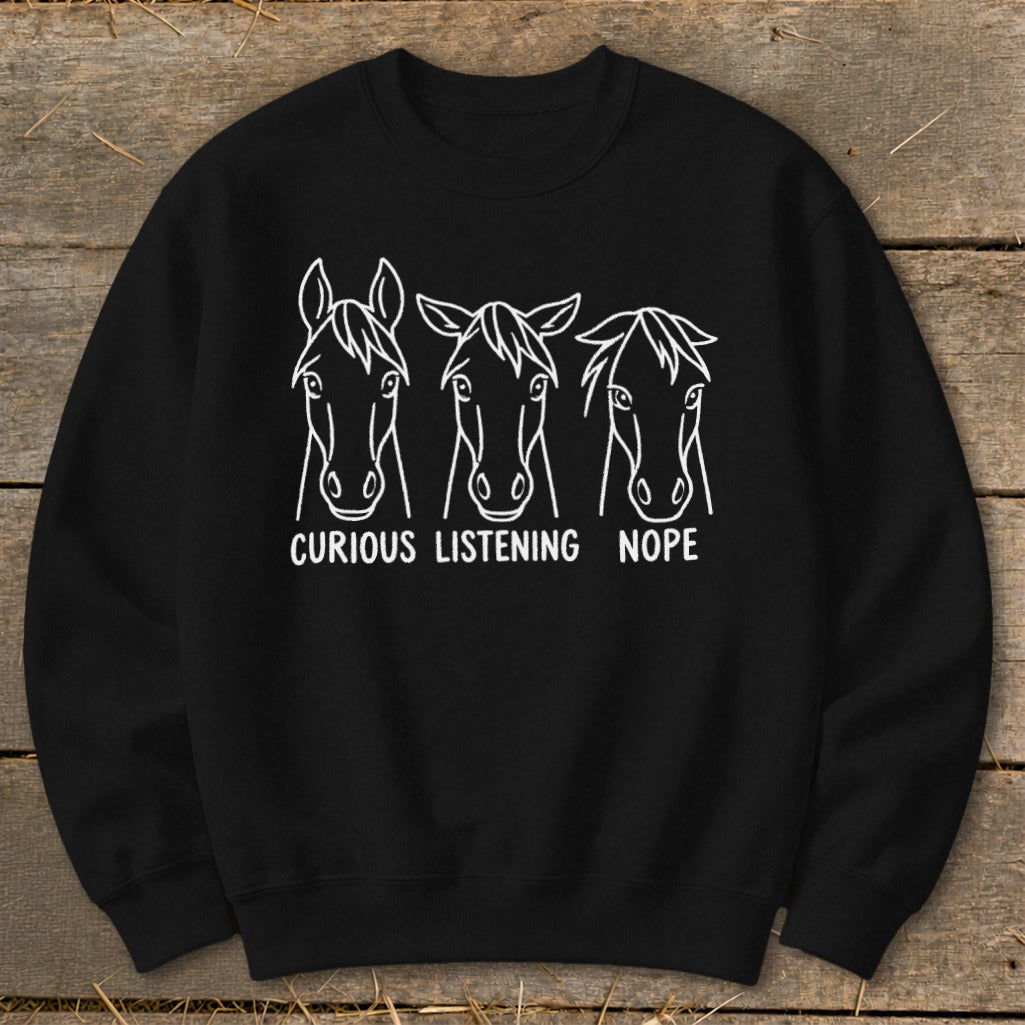 Black crewneck sweatshirt featuring a white line graphic of three horses with the captions Curious, Listening, and Nope.