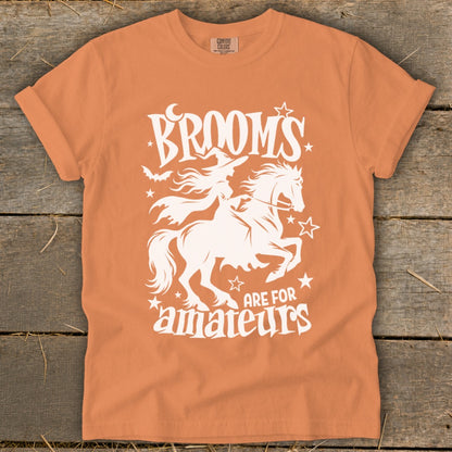 Orange t-shirt with white graphic of a witch on a horse, bats, and text.