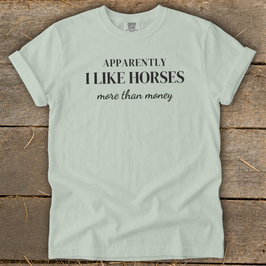 Pale green t-shirt with black text: "APPARENTLY I LIKE HORSES more than money."