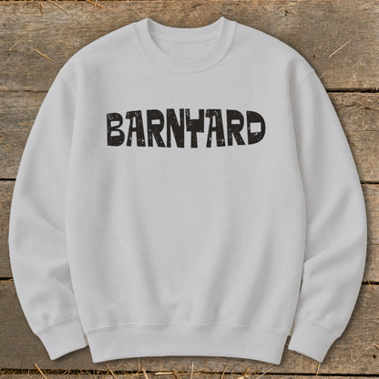 A light gray crewneck sweatshirt laid flat on a wooden background, featuring the distressed black text "BARNYARD" centered on the chest.