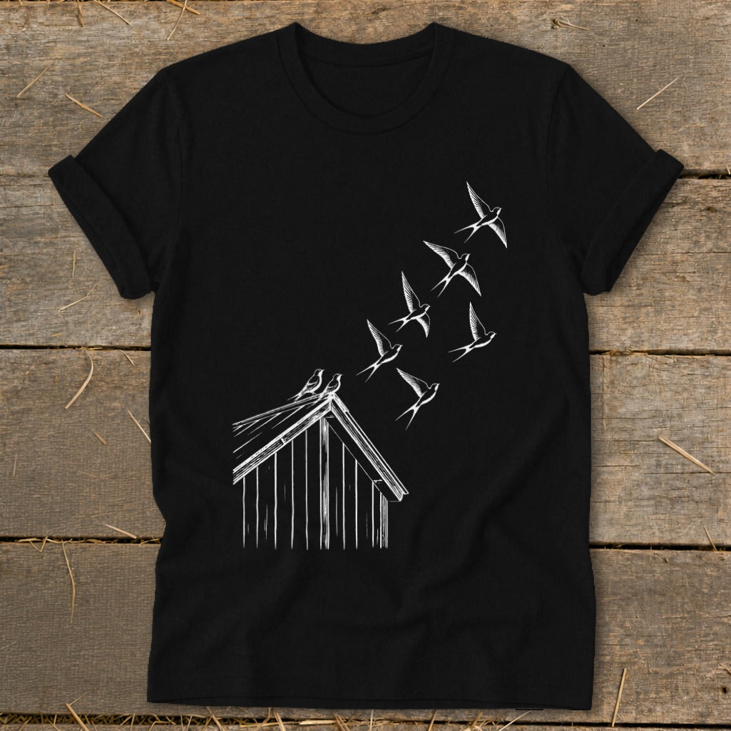 A black t-shirt featuring a white graphic of birds flying from a small wooden shed roof.