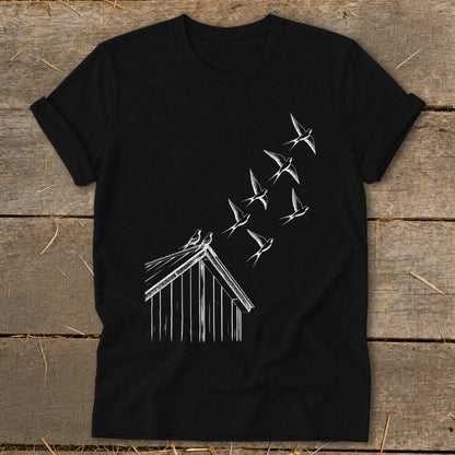 A black t-shirt featuring a white graphic of birds flying from a small wooden shed roof.