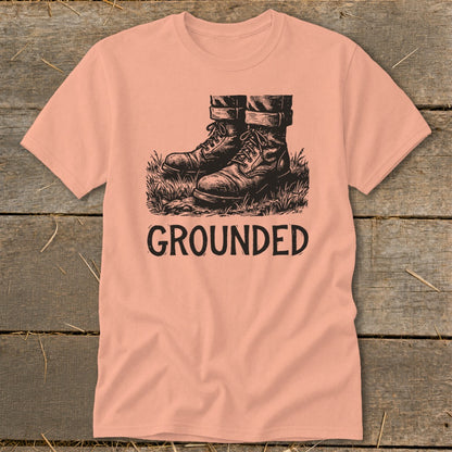 Peach t-shirt with black ink drawing of boots in grass and the word GROUNDED.
