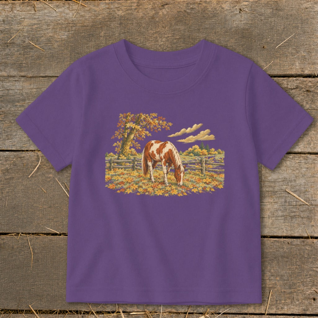 A short-sleeved purple t-shirt featuring a detailed embroidered patch of a brown and white horse grazing in an autumn pasture.