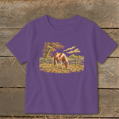 A short-sleeved purple t-shirt featuring a detailed embroidered patch of a brown and white horse grazing in an autumn pasture.