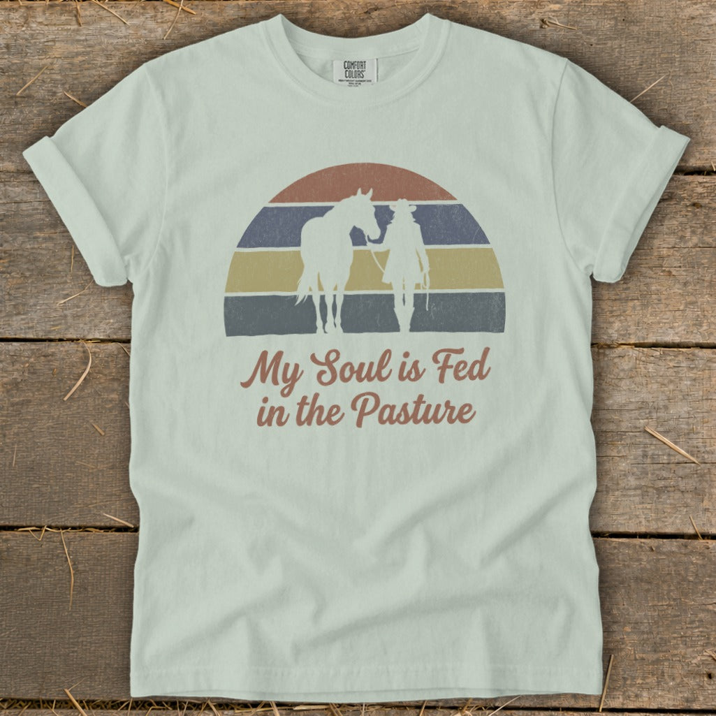 T-shirt with cowboy and horse silhouette, sunset graphic, and text "My Soul is Fed in the Pasture".