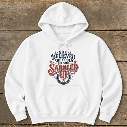 White hoodie with text "She believed she could so she saddled up" and horseshoe graphic.