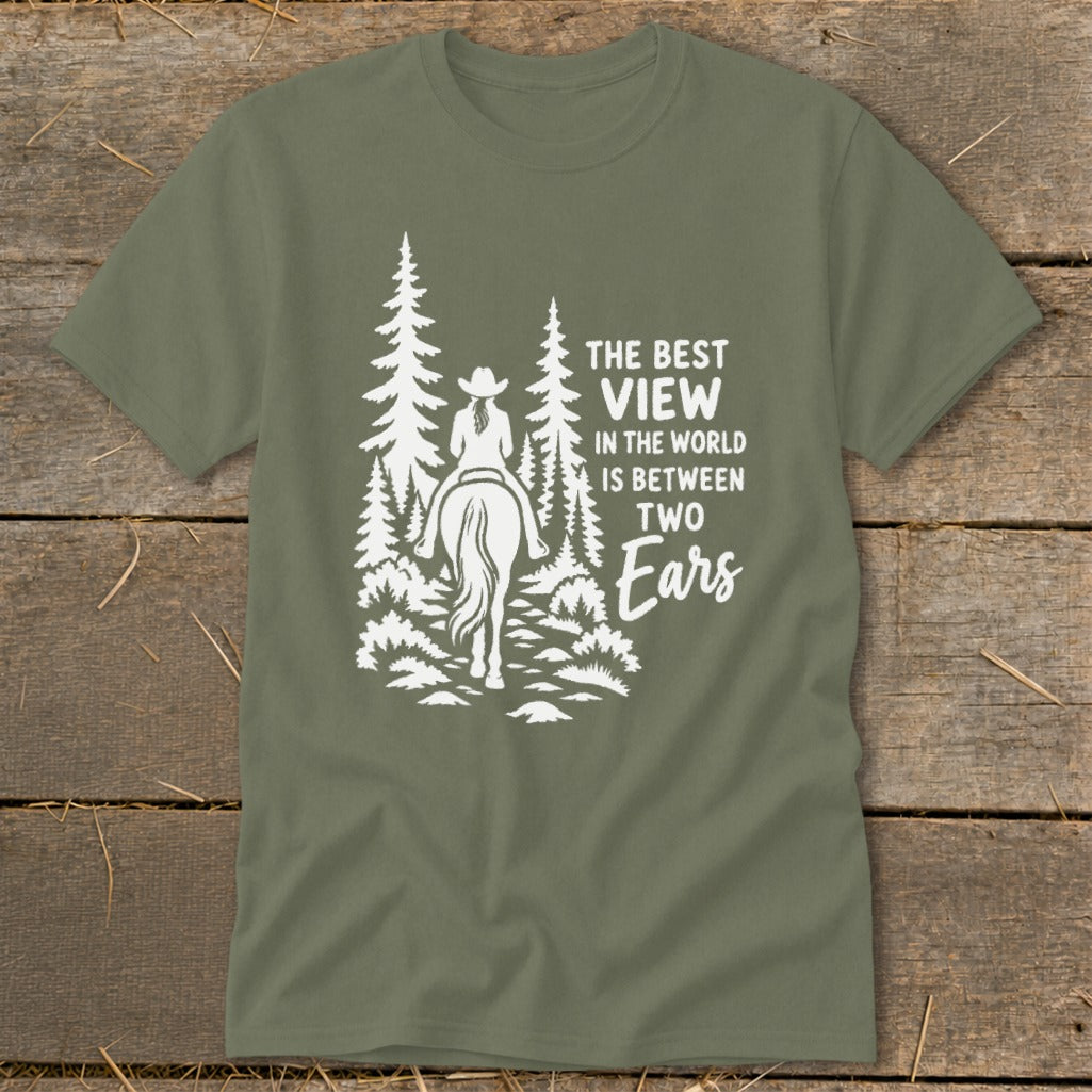 An olive green t-shirt with white graphic text reading The Best View in the World is Between Two Ears alongside a horse rider in a forest.