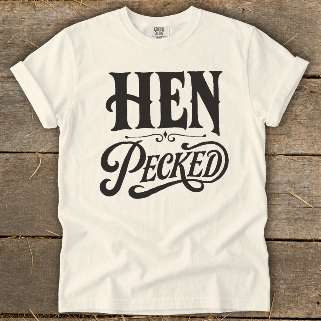 Cream t-shirt with black text reading "HEN PECKED" in decorative fonts.