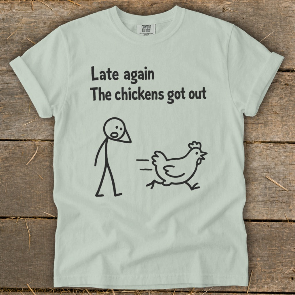 Light green t-shirt with black text "Late again. The chickens got out." and stick figure chasing a chicken.